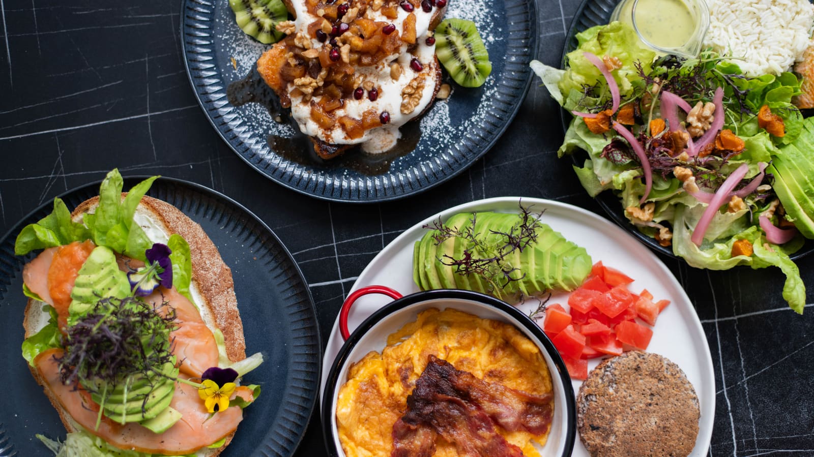 Avocado toast, ensalada y huevos con tocino recién servidos
